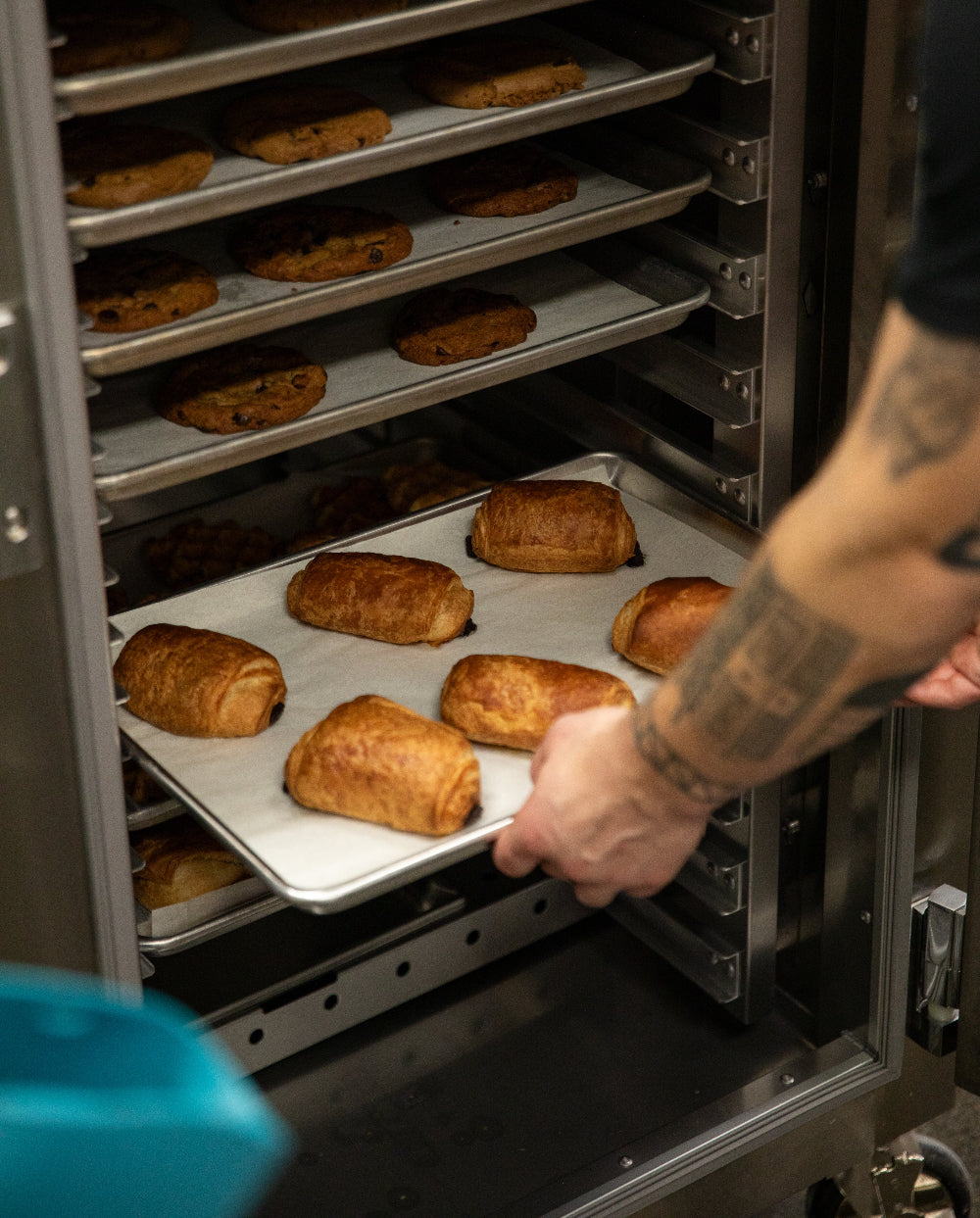 Person removing a tray of baked pastries from an oven.
