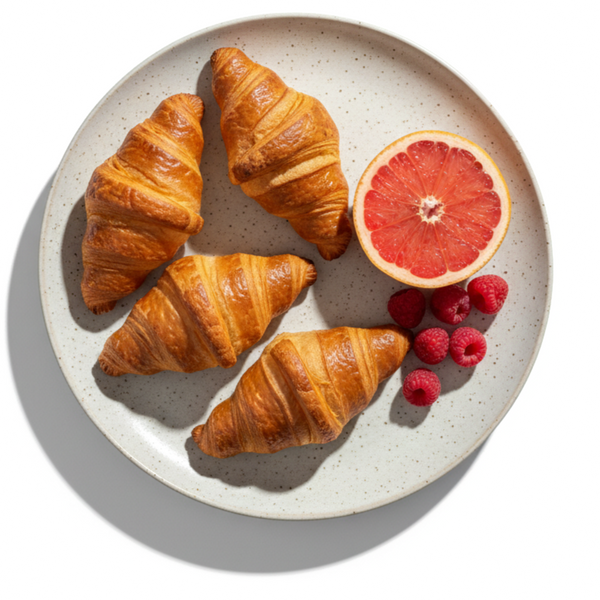 Four croissants on a plate with a half grapefruit and raspberries on a white background