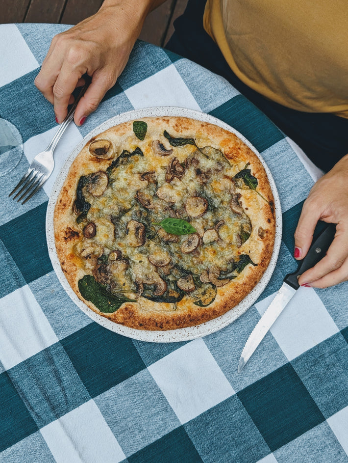 Slow-Fermented Veggie Pizza topped with mushrooms and spinach on a white plate