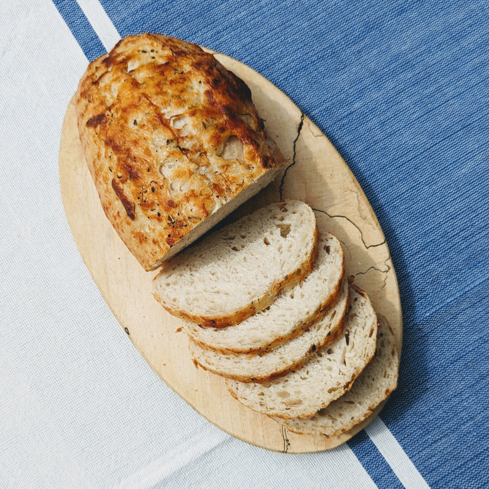 Sliced rustic herb loaf on an oval wooden cutting board over blue-and-white striped linens