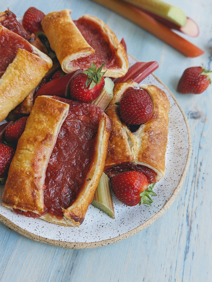 Strawberry Rhubarb Turnovers on a plate with fresh strawberries and rhubarb