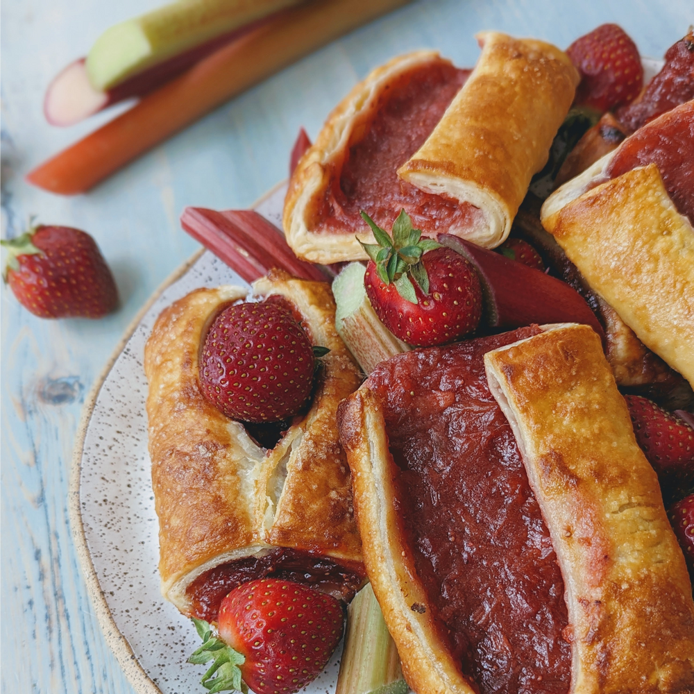 Rhubarb and strawberry puff-pastry tarts on a speckled plate with fresh strawberries and rhubarb stalks