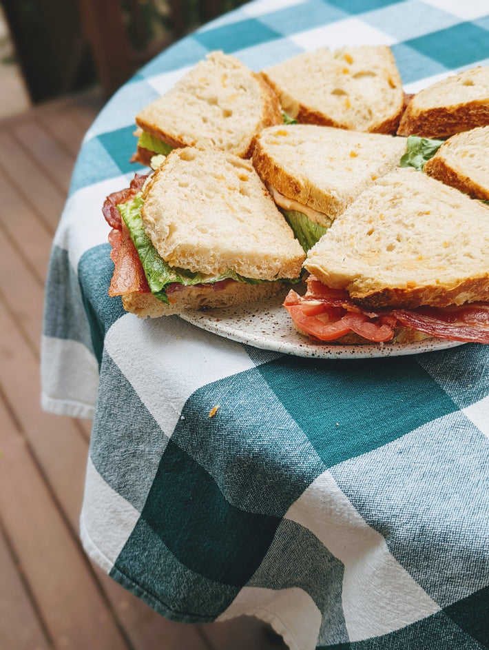 A plate of sliced sandwiches with lettuce and meat on a checkered tablecloth