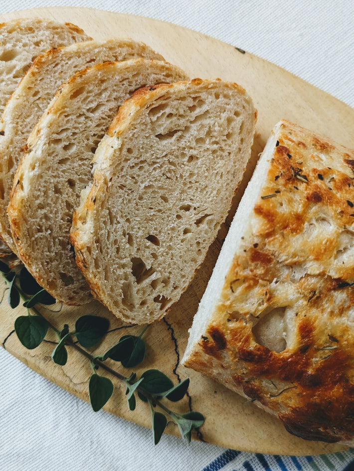 Sourdough bread with slices arranged on a wooden board, garnished with herbs