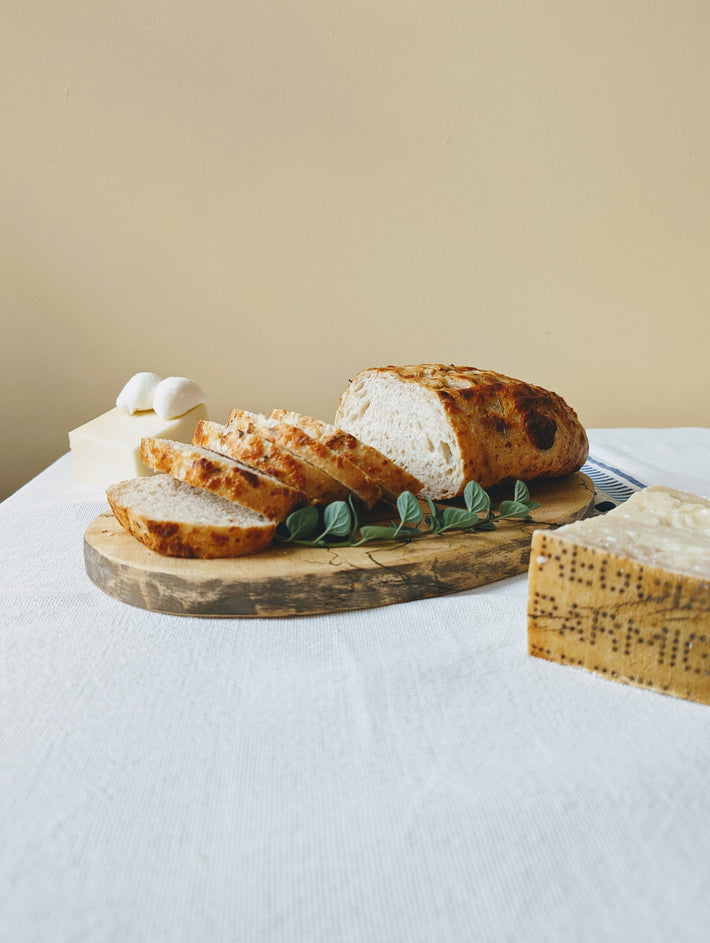 Sliced sourdough bread on a wooden board with cheese and eggs in the background