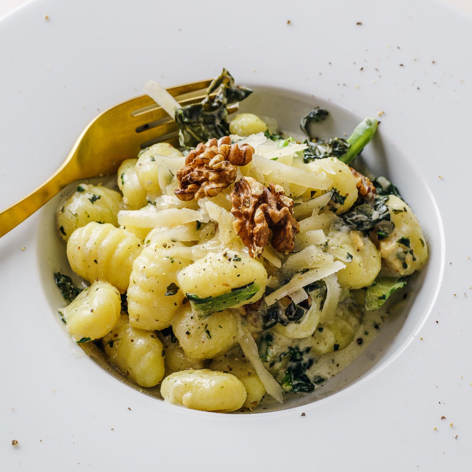 Potato gnocchi with greens and walnuts in a white bowl