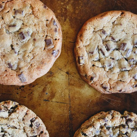 Four plant-based giant chocolate chip cookies on a brown baking sheet.