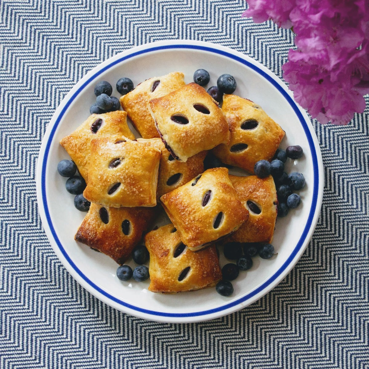 A plate of Wildgrain Blueberry Pie Bites surrounded by fresh blueberries