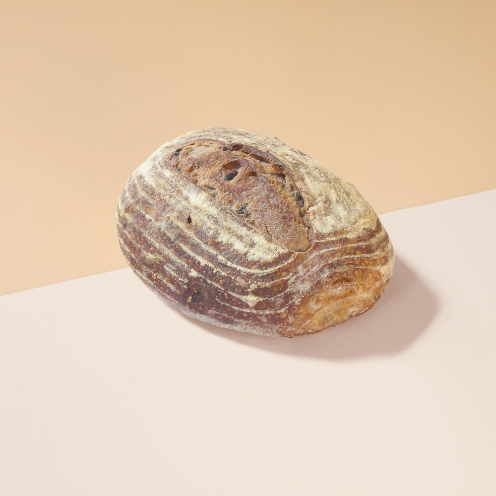 Round rustic sourdough loaf, flour-dusted with ridged crust, resting on a pale pink and peach surface.