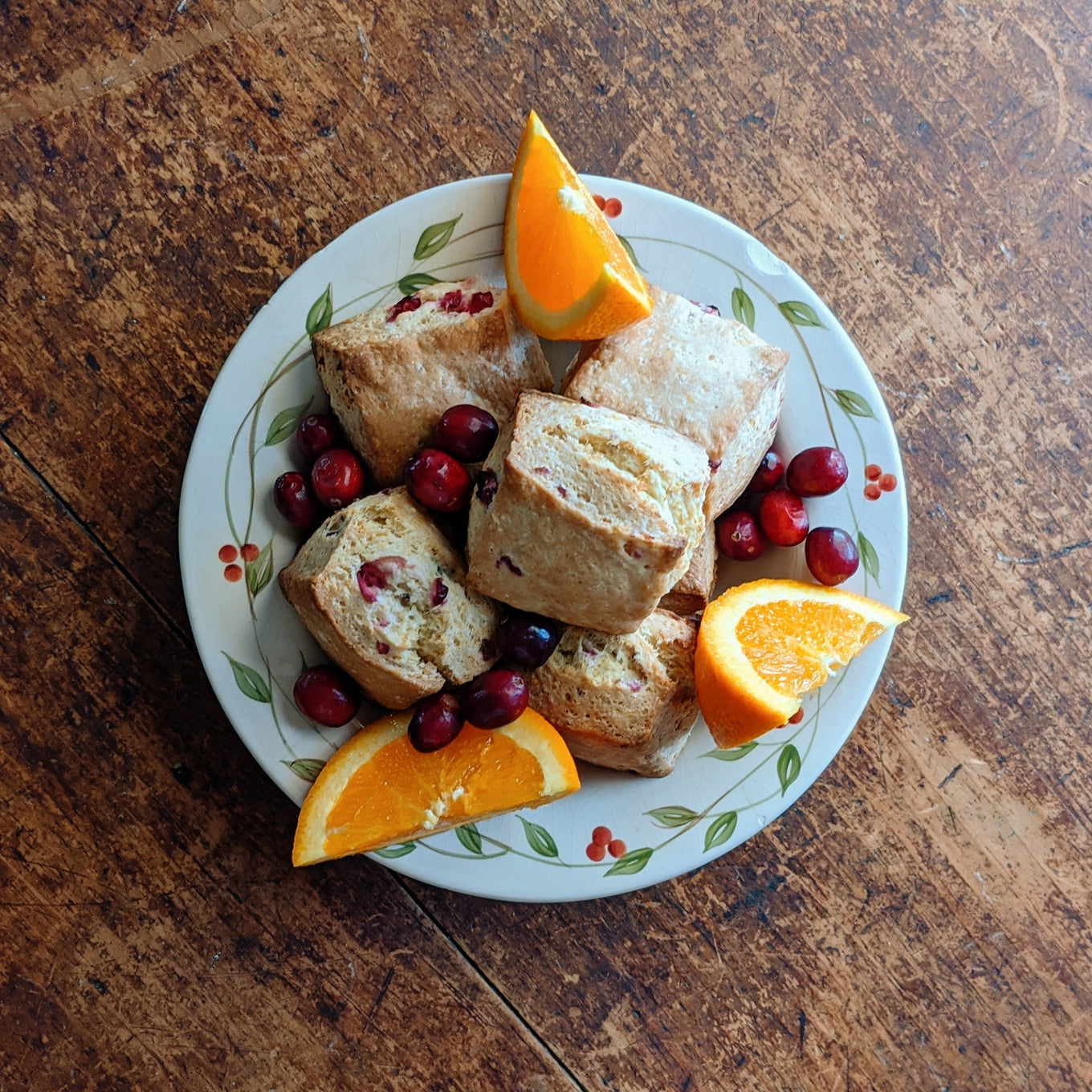 Plate of cranberry scones with fresh cranberries and orange wedges on a wooden table.