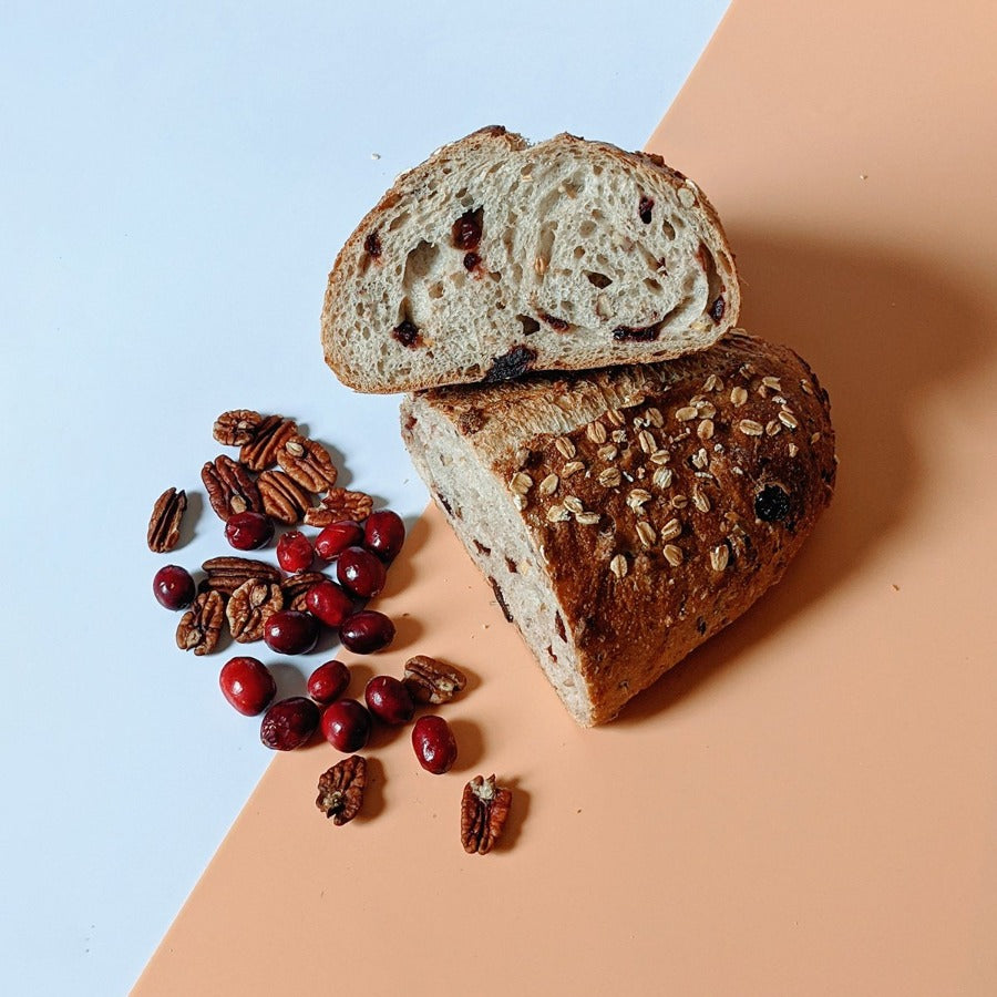 Sliced Slow-Fermented Cranberry-Pecan Loaf with pecans and cranberries on a colored background