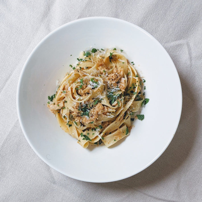 Top-down of Fresh Fettuccine in a white bowl showcasing hand-cut ribbons with grated cheese and parsley on a light cloth