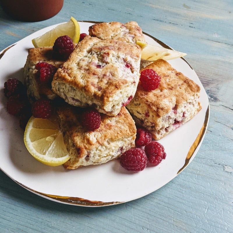 Lemon-raspberry scones stacked on a white plate with lemon wedges, on a light blue wooden table