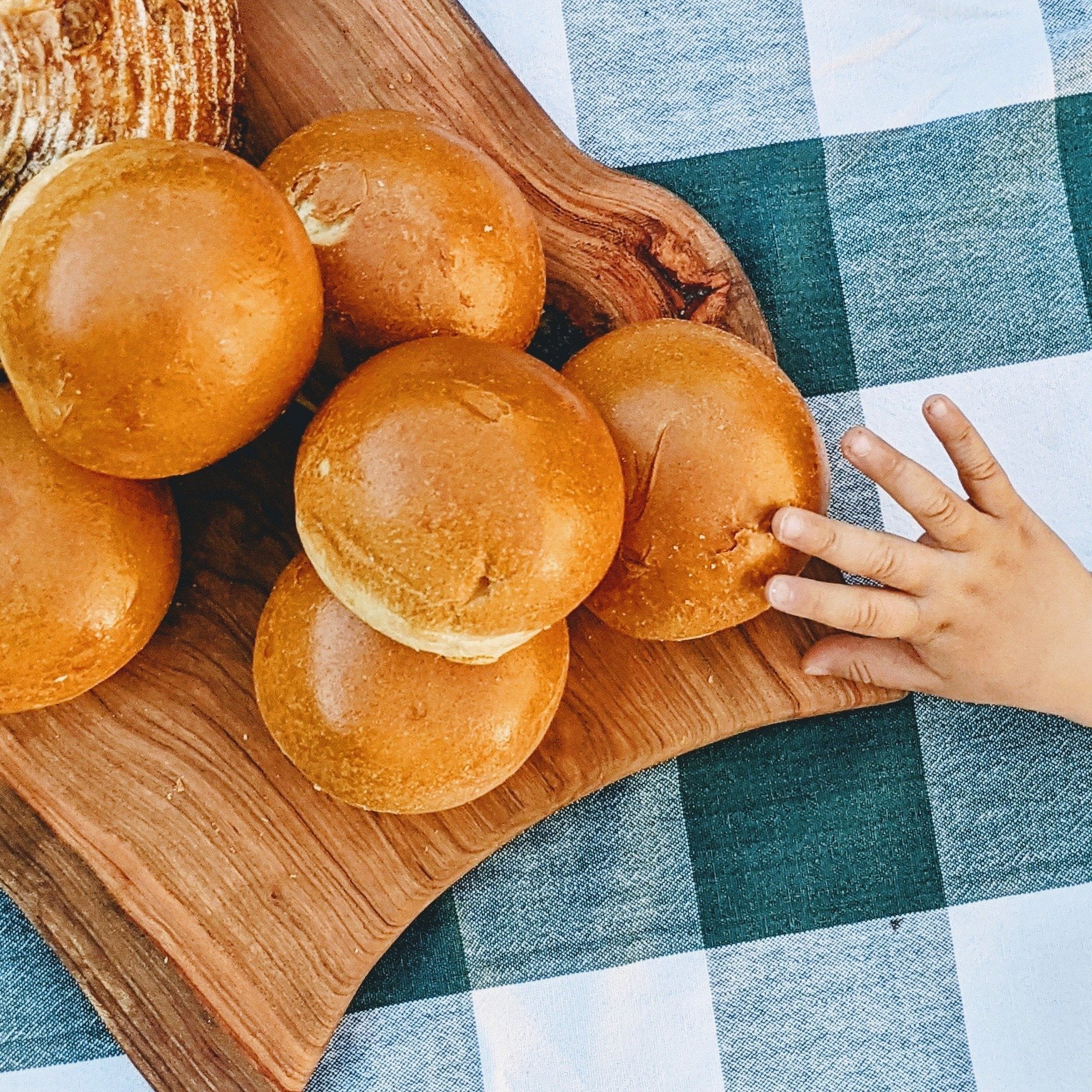 A wooden board with Slow-Fermented Brioche Rolls and a child's hand reaching for one.
