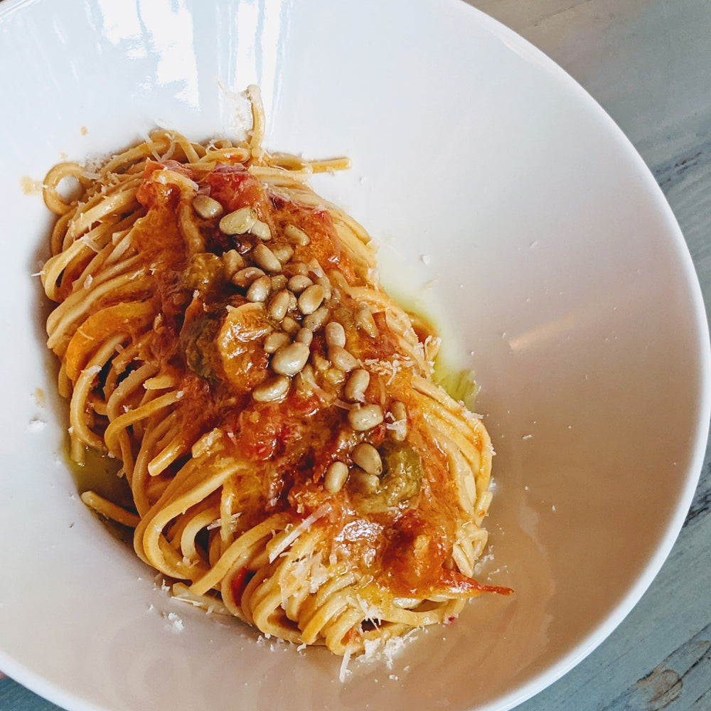 Plated pasta with tomato sauce and pine nuts on a white plate.