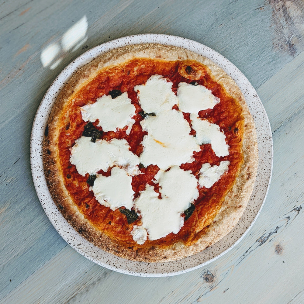 A round Slow-Fermented Margherita Pizza topped with dollops of mozzarella cheese on a rustic plate.