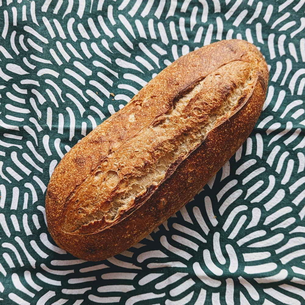 A rustic spelt sourdough loaf on a patterned cloth background.