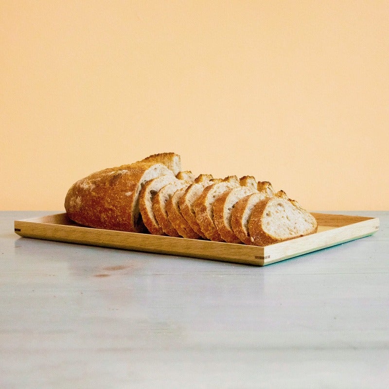 Sliced artisan loaf on a wooden tray on marble countertop with pale peach background