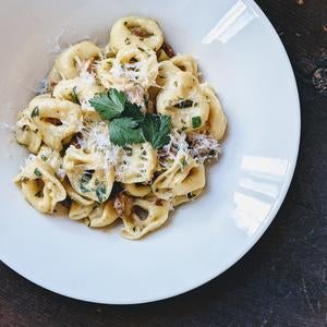 White plate of cheese-filled tortellini garnished with grated cheese and parsley on a dark wooden table.
