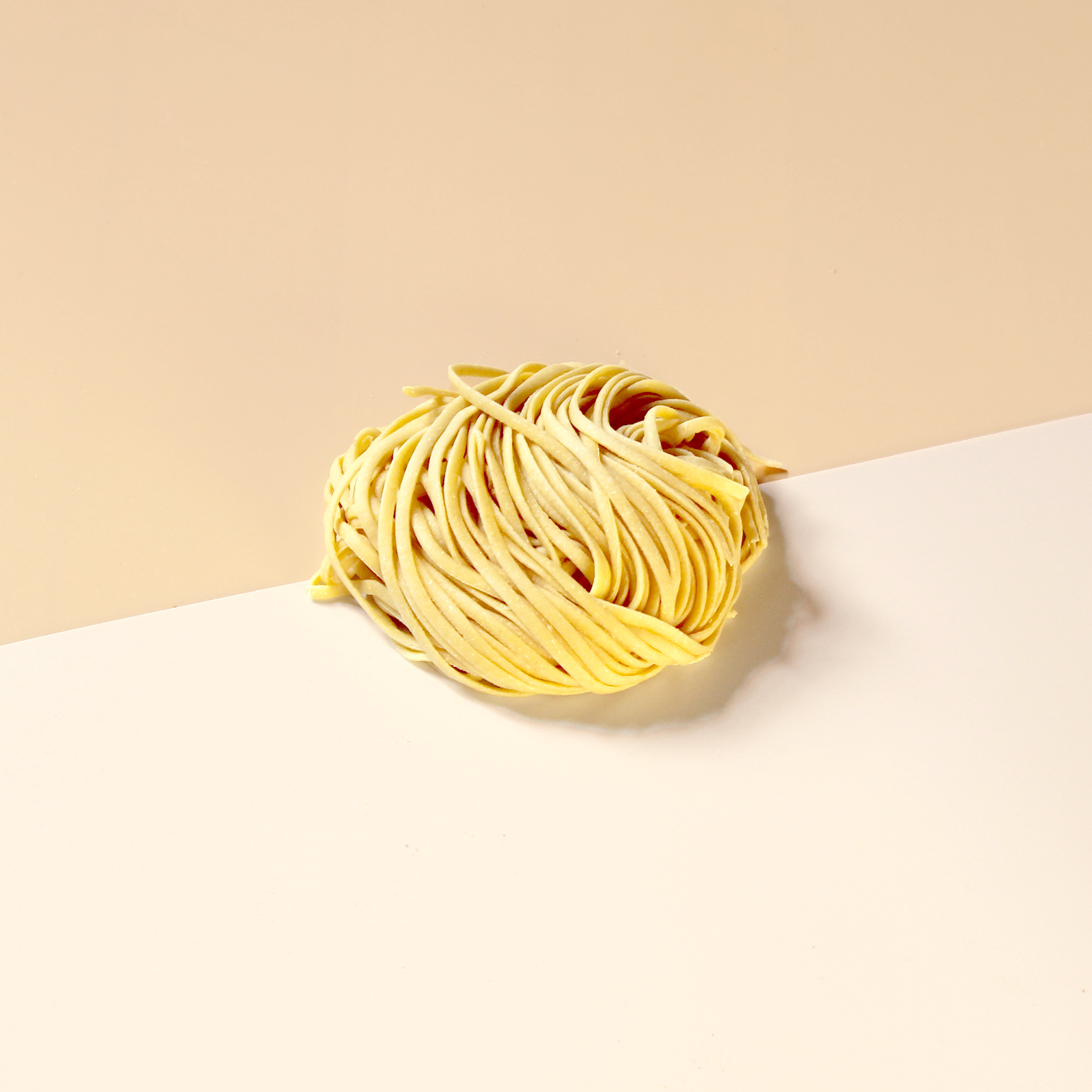 Nest of uncooked tortellini pasta on a two-tone beige and cream background