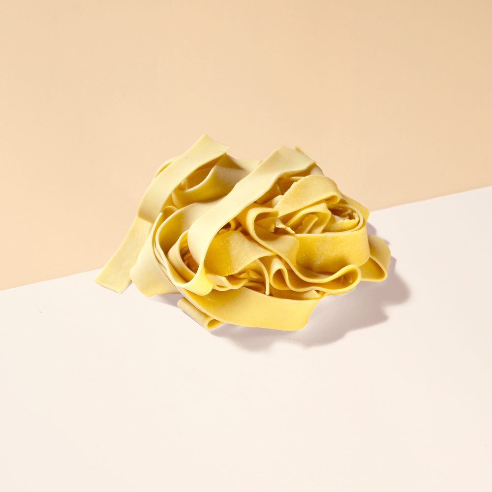 Nest of uncooked yellow pasta ribbons on a two-tone beige and white surface
