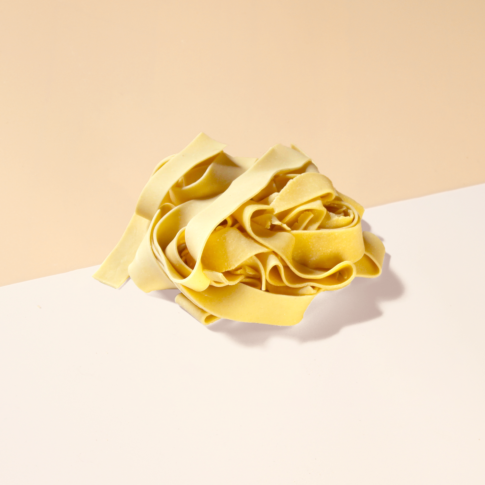 Nest of uncooked yellow pasta ribbons on a two-tone beige and white surface