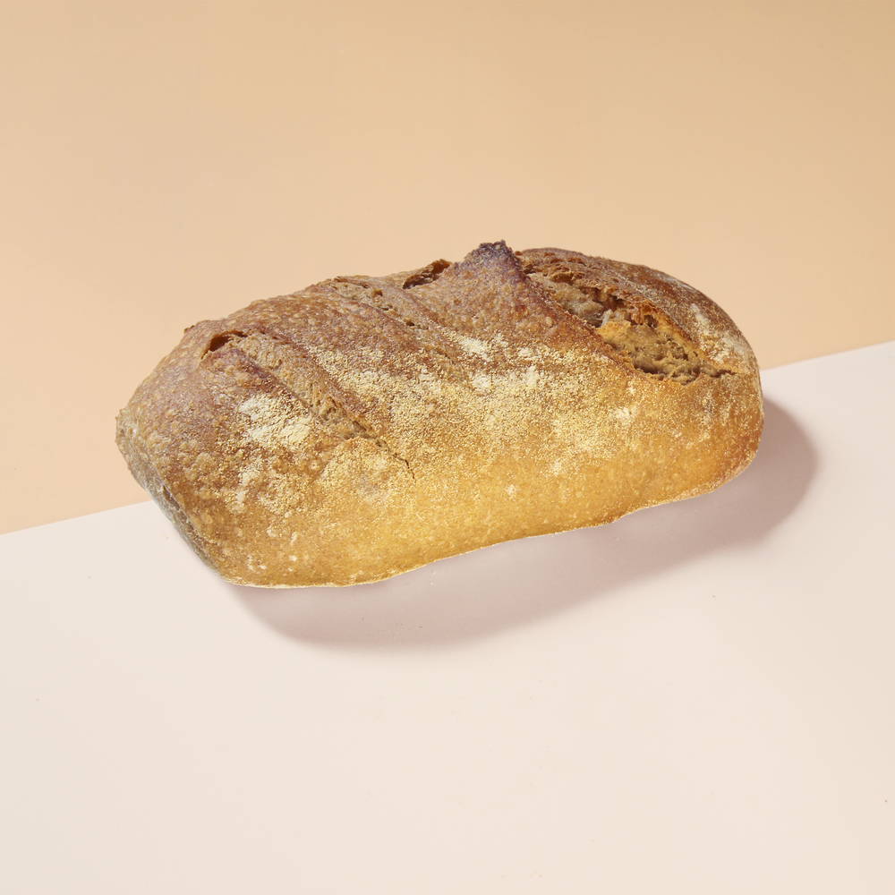 Crusty artisan loaf of rustic sourdough bread on a two-tone pale pink and beige surface